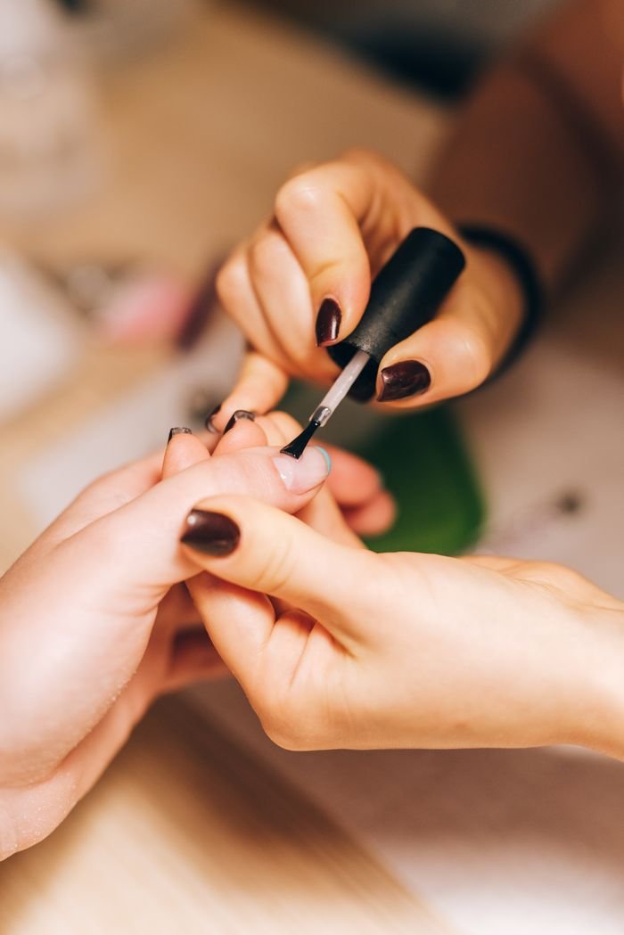 about-01 Close-up of a manicurist applying nail polish during a professional manicure session.