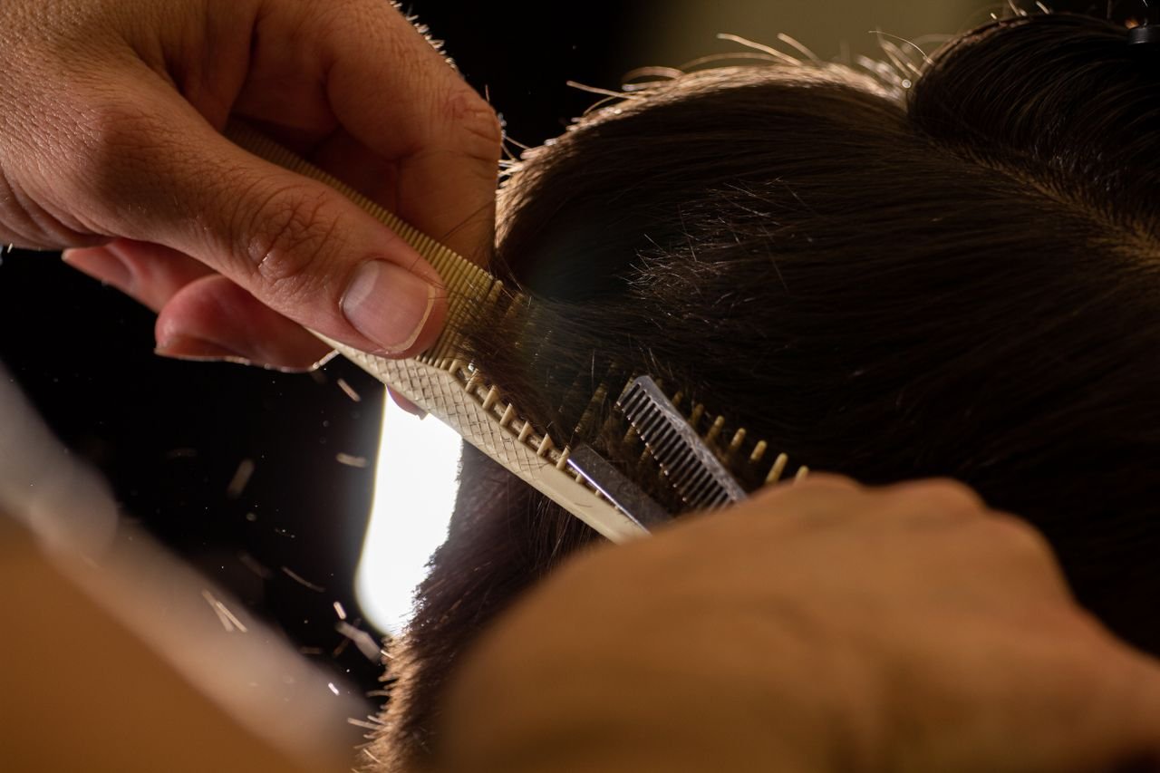 our-experience Close-up of a stylist trimming hair with a comb and scissors indoors.