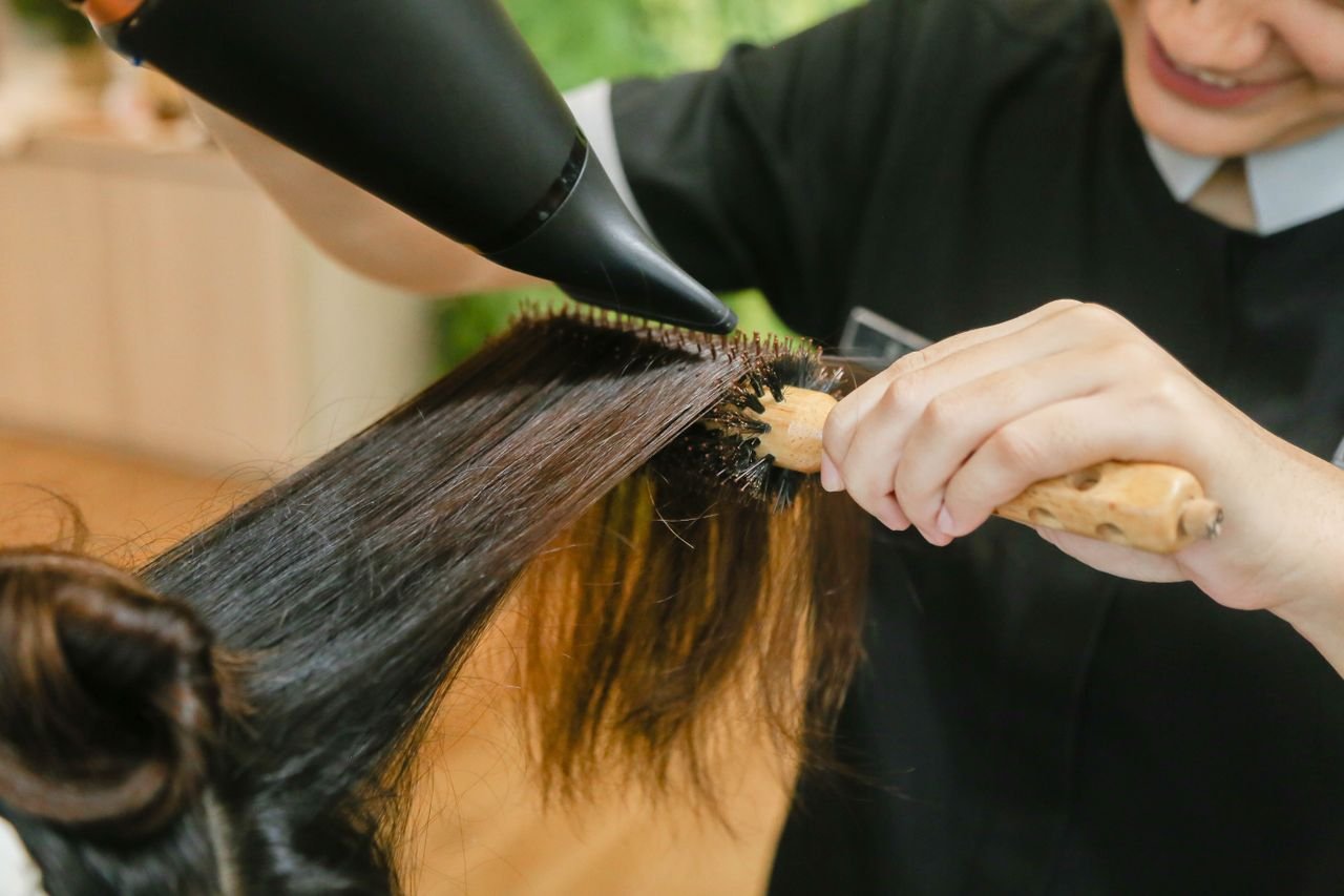 services-03 Close-up of hair stylist using a hairdryer and brush to style long hair.